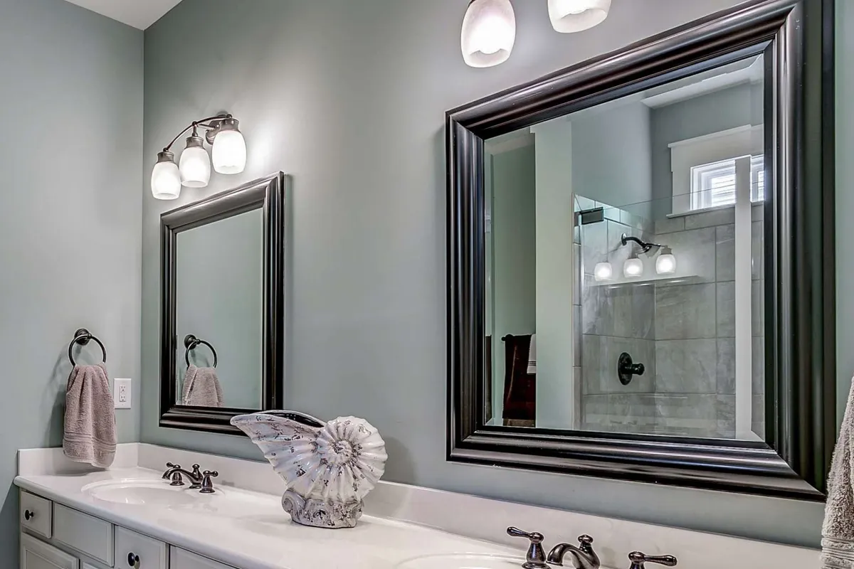 A bright bathroom featuring double sinks, large mirrors, and a decorative shell accent. The room is bathed in natural light, creating a refreshing and inviting environment perfect for shared or private morning rituals.