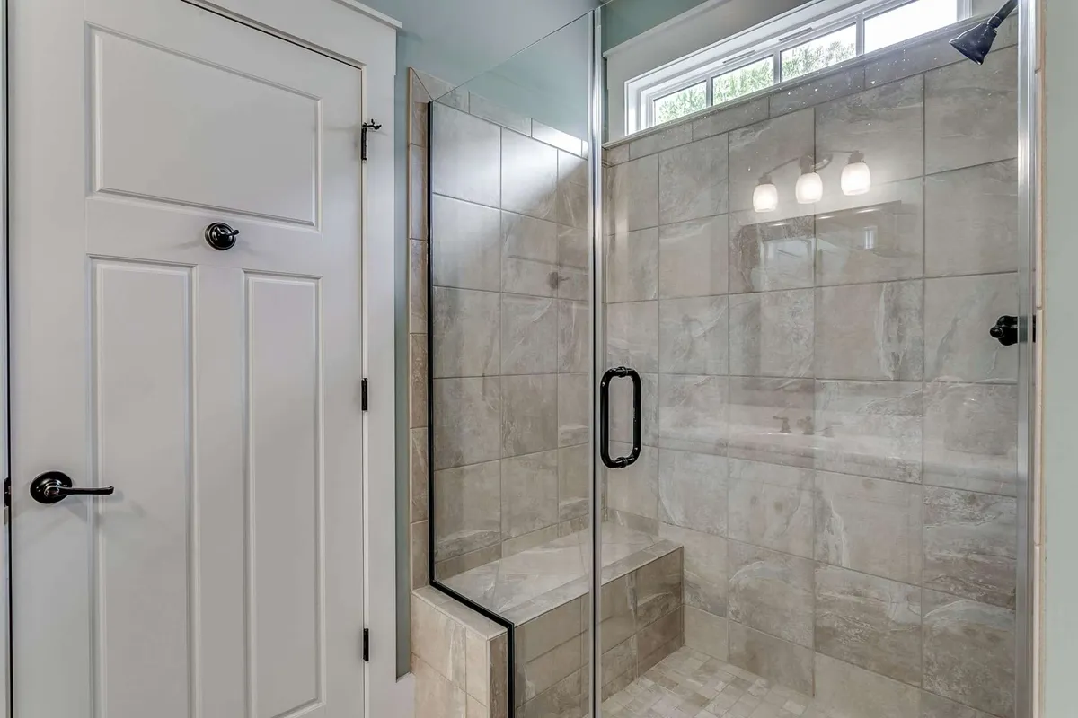 A modern bathroom with a glass shower enclosure, tiled walls, and a built-in bench seat. The clean lines and inviting atmosphere suggest a space designed for refreshing self-care routines and winding down after an active day.