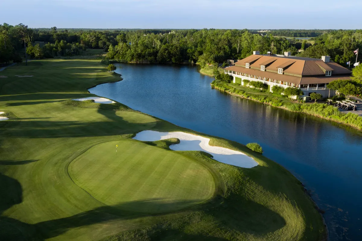A sweeping view of a lush golf course beside a tranquil lake and elegant clubhouse, set under an open sky. The landscape suggests space for group picnics, friendly golf games, and serene strolls together, embodying leisure and connection with nature.
