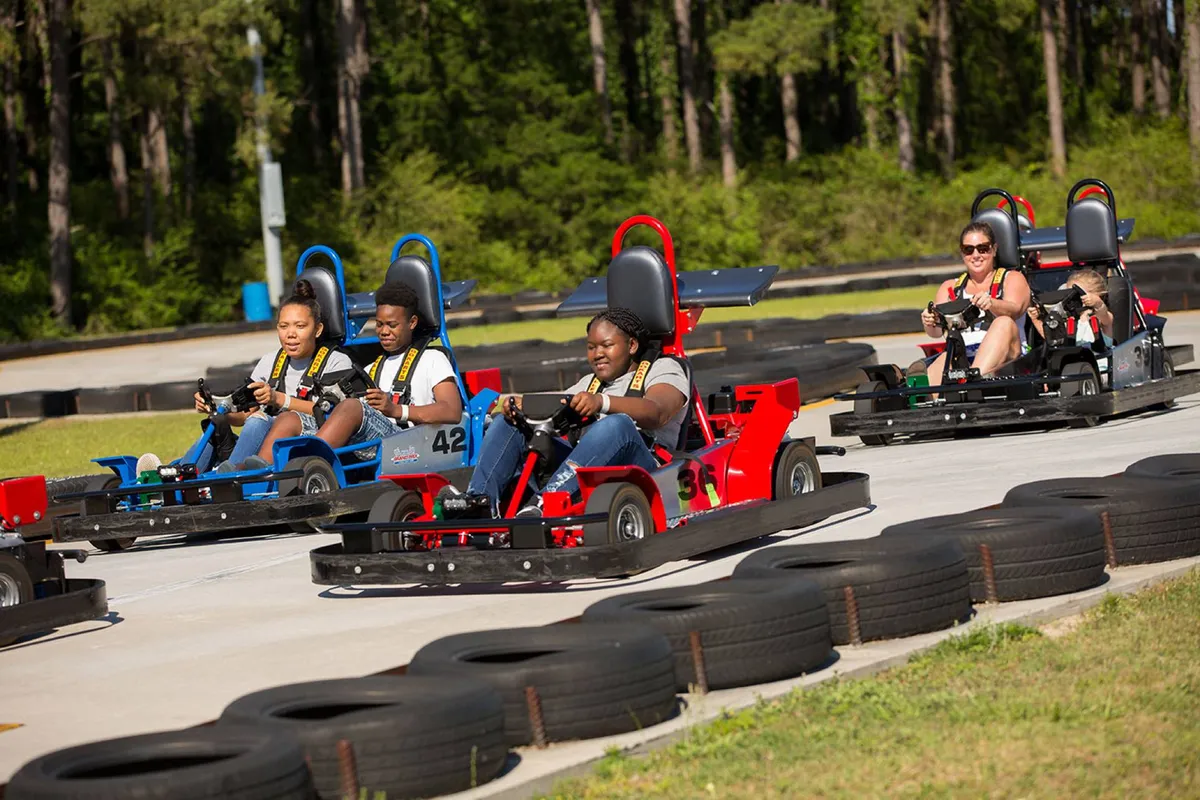 A playful scene at an outdoor go-kart race track, featuring several go-karts, participants racing, and the energetic atmosphere of friendly family competition.