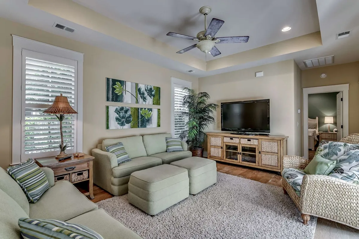 The image showcases the inviting living room of a single-family house in North Myrtle Beach. A plush sofa faces a modern coffee table and large television, surrounded by vibrant artwork and a lush green plant, creating a comfortable and stylish setting for relaxing, socializing, or unwinding after a day at the beach.