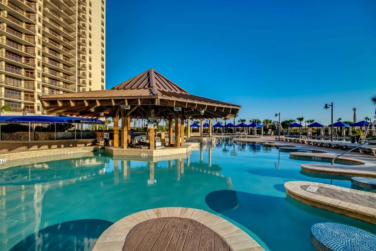 An inviting outdoor swimming pool area surrounded by palm trees, with a charming gazebo and plenty of lounge chairs. The setting is vibrant and ideal for group gatherings, featuring sunset lighting that enhances the vacation atmosphere. The pool area is clearly designed for both relaxation and group socializing, perfect for days spent in the resort community.